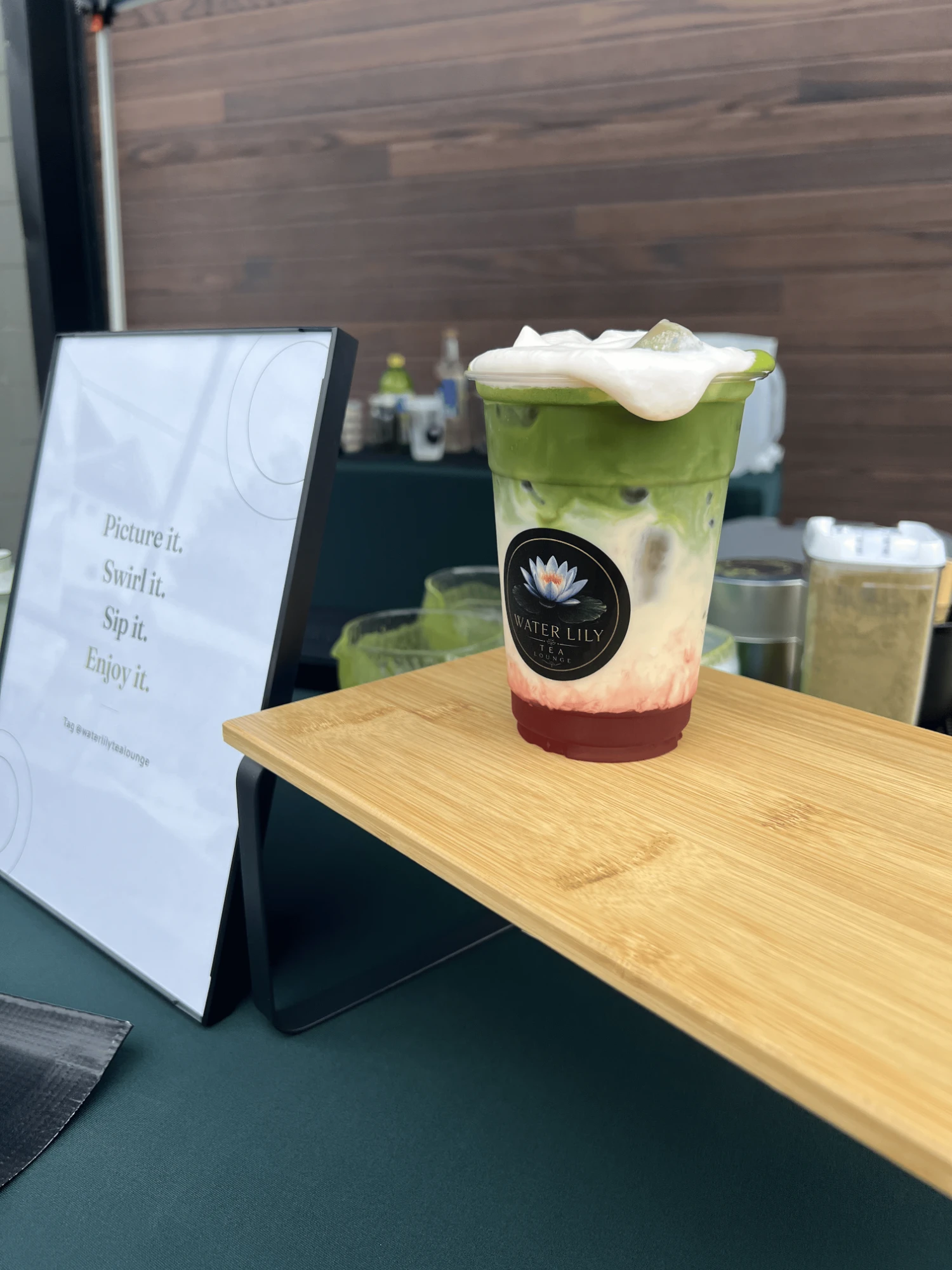 A Water Lily matcha strawberry latte topped with cream on a bamboo tray